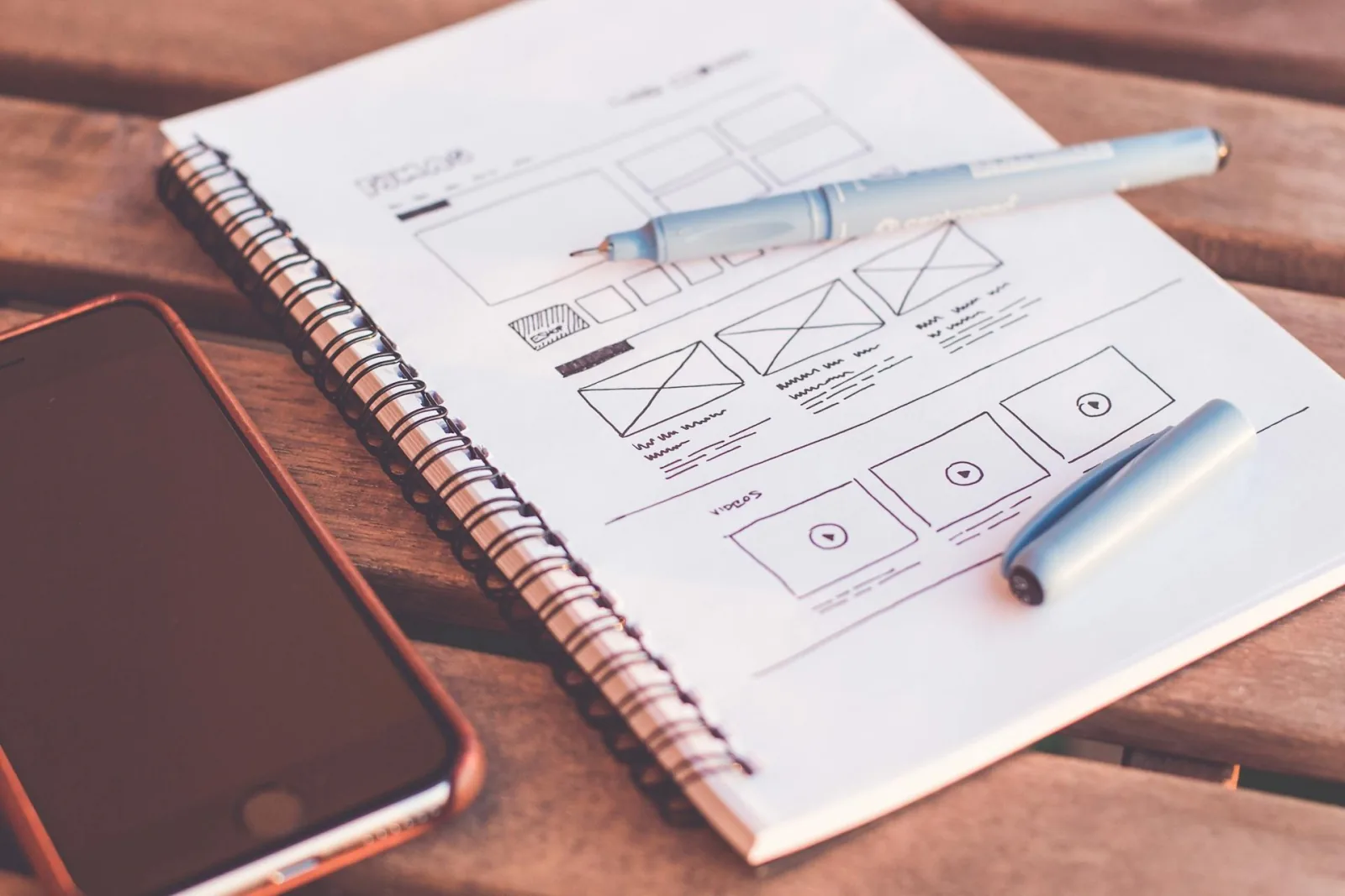 From Syllabus to Sales Page: Write Copy That Converts image Hand-drawn website wireframe in notebook beside phone, planning sales page copy