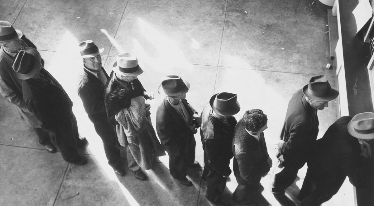 (still image) Unemployment benefits aid begins. Line of men inside a division office of the State Employment Service office at San Francisco, California, waiting to register for benefits on one of the first days the office was open, (1938)